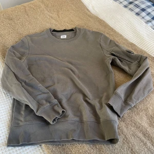 Grå sweatshirt från C.P. Company - Säljer en stilren grå sweatshirt från C.P. Company i mycket bra skick. Inte använd på många år då den är för liten. Den sitter true to size!