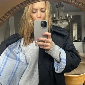 Svart quiltad jacka från Ganni - Säljer en superfin svart quiltad jacka från Ganni. Den har en oversized passform och är perfekt för höst och vår. Jackan har långa ärmar och en snygg krage. Insidan är fodrad med ett stilrent blått och vitt randigt mönster. Perfekt för att hålla stilen när det är lite kyligare ute!
