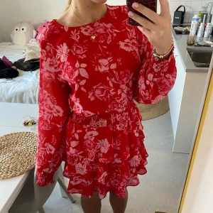 Blommig volangklänning - Säljer en superfin röd klänning med blommigt mönster och volanger från Gina tricot🩷🩷Den har långa ärmar och en smockad midja som ger en fin passform. Perfekt för sommarens fester🌟Klänningen är i mycket bra skick! Storlek 40 och skulle säga L🫶