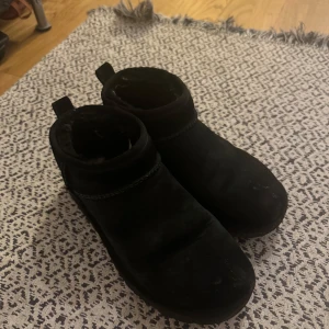 Svarta Uggs  - Säljer ett par svarta uggs. De är i bra skick med lite slitage på sulorna. Perfekta för höst och vinter med en stilren design. De har en praktisk dragflik baktill för enkel påtagning.