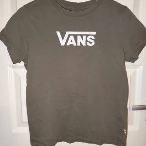 Gråbrun t-shirt från Vans - Säljer en snygg t-shirt från Vans i storlek medium. Den har en klassisk design med korta ärmar och det ikoniska Vans-loggan i vitt på framsidan. Perfekt för vardagsbruk eller att chilla i. Skön och stilren, passar till det mesta! 🛹