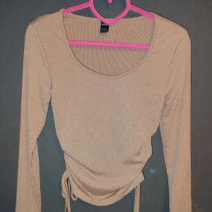 Beige ribbad topp från SHEIN - Säljer en snygg beige ribbad topp från SHEIN i storlek S. Den har långa ärmar och en cool knytdetalj i midjan som ger en fin passform. Perfekt för både vardag och fest! 🥳