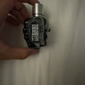 Parfymflaska från Diesel - Säljer en cool parfymflaska från Diesel formad som en knytnäve. Flaskan är genomskinlig med en silvrig kork och har en modern och edgy design. Perfekt för den som vill ha en unik och stilren parfymflaska i sin samling!