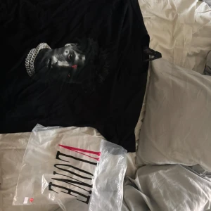 Svart t-shirt med tryck från VLONE - Säljer en svart t-shirt från VLONE i storlek L. Den har ett coolt tryck på framsidan och ett stort rött 'V' på baksidan. Gjord av 100% bomull, så den är riktigt skön att ha på sig. Perfekt för en avslappnad stil eller att bära på fest!