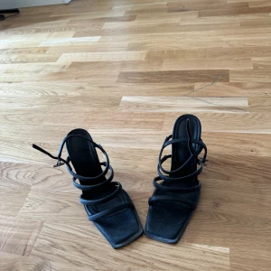 Svarta klackskor med remmar - Säljer ett par eleganta svarta klackskor med flera tunna remmar som ger en stilren look. Skorna har en spetsig tå och en smal klack som ger en snygg siluett. Perfekta för festliga tillfällen eller en utekväll.