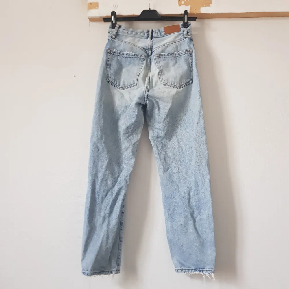 Säljer ett par ljusblå jeans från Gina Tricot i storlek 34. De har en klassisk straight fit och är tillverkade i denim. Jeansen har slitning på framsidan och längst ner.. Jeans & Byxor.