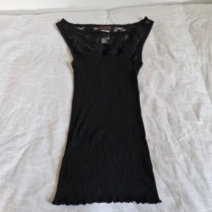 Svart ribbad topp från Rosemunde - Säljer en snygg svart ribbad topp från Rosemunde. Den är ärmlös och har fina spetsdetaljer vid halsringningen. Fantastiskt fin sammansättning - 70% silke, 30% bomull! Figurframhävande passform. Perfekt för både vardag och fest!