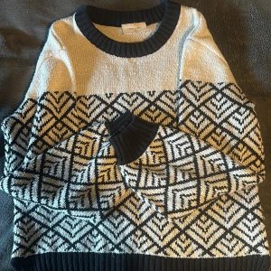 Mönstrad stickad tröja från Free/Quent - Säljer en superfin stickad tröja från Free/Quent i storlek XS. Den har ett snyggt geometriskt mönster i svart och beige, perfekt för höst och vinter. Tröjan är långärmad med ribbade muddar och nederkant. Den är både varm och stilren, perfekt för kyliga dagar!