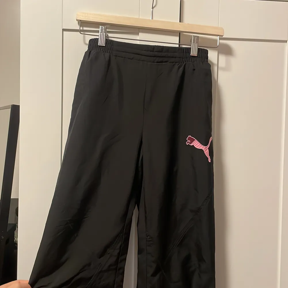 Säljer ett par svarta byxor från Puma med en rosa logga på sidan. Byxorna har en loose passform och är högmidjade med resår i midjan för extra komfort. Perfekta för en avslappnad stil eller träning. Köpt för 399kr säljer för endast 100kr!. Jeans & Byxor.