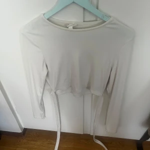 Långarmad croptop med band - Det är en vit långarmad croptop med band som går runt midjan säljer pga att den är för stor och är använd bara en gång❤️❤️