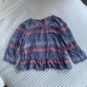 Mönstrad blus med volang  - Mönstrad blus med volang längst ner, små knappar på ryggen och trekvartsärmar. Ett litet hål längst ner i volangen på ryggen. 