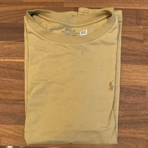 Beige t-shirt från Polo Ralph Lauren - Säljer en snygg beige t-shirt från Polo Ralph Lauren. Den är i bra skick, inte använd jätte mycket. Liten defekt på framsidan (se bild 5). Hör av dig vid eventuella frågor. 