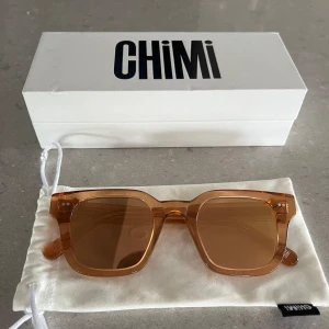 Bruna solglasögon från Chimi - Säljer ett par snygga solglasögon Chimi 004/peach. De har en fyrkantig form och är gjorda av ett transparent  material som ger en cool retrovibe. Perfekta för sommardagar och att matcha med olika outfits. Kommer med en vit förvaringspåse och case.