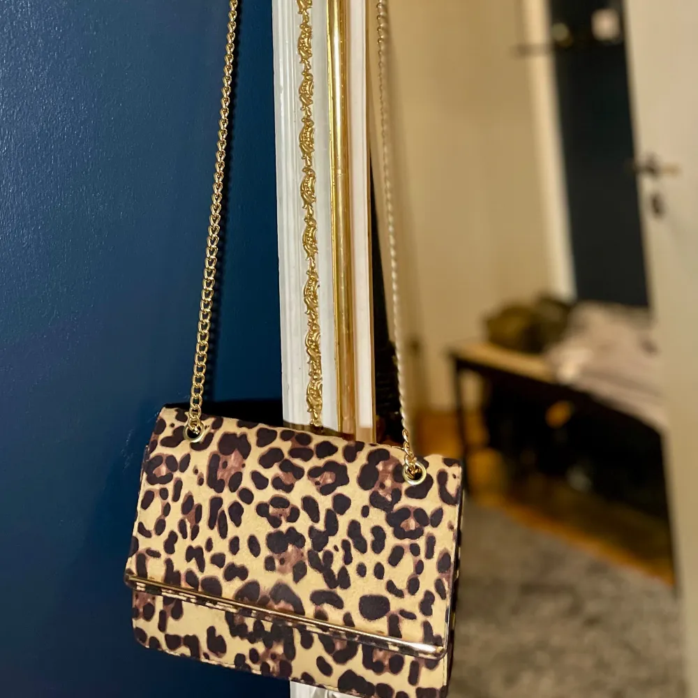 En snygg väska i leopard med gulddetaljer från New Look🐆✨Använd en gång, som ny!  Mått: B:22 cm H:16 cm. Kan hänga över axeln i två lägen, kort och lång.. Väskor.