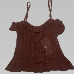 Brun stickad topp - Söt brun stickad topp med volanger. Toppen är i en mjuk och skön kvalitet och är helt oanvänd. Passar storlek S-M!