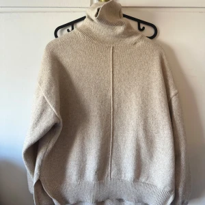 Beige polotröja i ull - Säljer en supermysig beige polotröja i ull. Den har en hög polokrage och långa ärmar, perfekt för kyliga dagar. Tröjan är oversized och har ribbade muddar vid ärmslut och nederkant. Perfekt för höst och vinter!