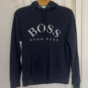 Hugo boss tröja med luva - Hugo boss tröja i marinblå färg med luva samt Hugo boss i broderat i vit framtill. Storlek M. Okej skick men något sliten på vissa ställen men inget man tänker på. Nypris: 1799kr