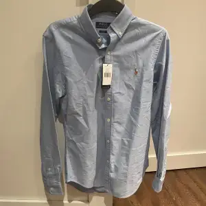 Säljer en snygg blå skjorta från Polo Ralph Lauren i slim fit. Skjortan är långärmad och är helt ny då lappen är kvar, säljer den då jag aldrig använder den och nu är den för liten