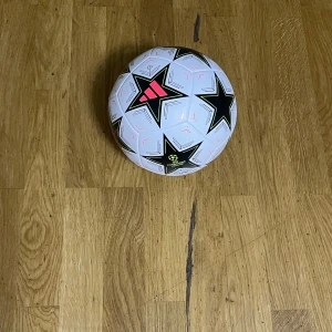 Vit Champions League boll - Säljer en vit fotboll från Adidas med ett coolt stjärnmönster i svart och röd detaljer. Perfekt för fotbollsträningen eller matchen. Champions League-logga syns tydligt på bollen.helt nytt skick har aldrig används 