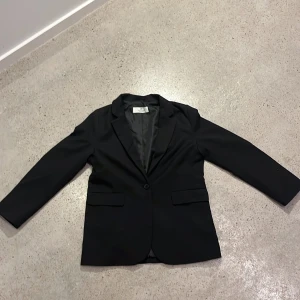 Svart kavaj från H&M - Snygg svart kavaj från H&M i storlek  140. Perfekt för en stilren look med klassiska slag och enkelknäppning. Kavajen har två fickor framtill och är helfodrad för extra komfort.