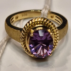 Guldpläterad ring med afrikanska amethyst - Elegant guldpläterad ring med en stor afrikanska amethyst i centrum. Ringen har en vacker, detaljerad infattning runt stenen som ger ett lyxigt intryck. Perfekt för att ge en färgklick till din outfit. Beskrivning: 18 ct guldpläterade 925 silver ring, sten: afrikanska amethyst 1,887 ct, storlek 15,6 mm  (K)
