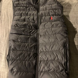Svart dunväst från Polo Ralph Lauren - Säljer en stilren svart dunväst från Polo Ralph Lauren. Västen har en dragkedja framtill. Riktigt fet. Storlek M köpte den för 3000