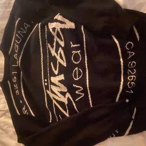 Stussy tröja - Snygg svart tröja från Stussy med vit text och grafiska detaljer. Perfekt för en avslappnad stil. Tröjan har långa ärmar och en klassisk passform.