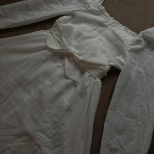 Vit klänning med knytband - Säljer en elegant vit klänning med långa ärmar och ett fint knytband i midjan. Klänningen har en smickrande passform och är perfekt för somriga tillfällen. Den är tillverkad i ett lätt och luftigt material som ger en bekväm känsla.