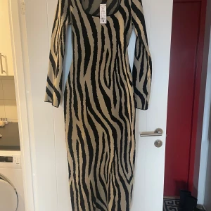 Zebramönstrad klänning från Ginatricot - Snygg zebramönstrad klänning från Ginatricot i beige och svart. Helt oanvänd med prislappen fortfarande kvar! Storlek M 
