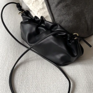 Svart axelväska  - Snygg svart axelväska med en minimalistisk design. Väskan har en justerbar axelrem och en stilren dragskoöppning. Storleken är mellan kuvertväska och en axelremsväska. Perfekt för en natt ute. Använts endast en gång, sparsamt då.💕Köpt för ett par år sedan och har inte kommit till användning! 