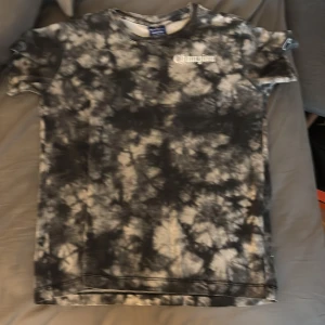 Svart och vit t-shirt från Champion - Cool t-shirt från Champion i svart och vit batikstil med texten 'get over it' på baksidan. Perfekt för en avslappnad stil. Kortärmad och tillverkad i mjukt material.