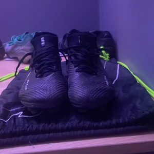 Svarta fotbollsskor från Nike - Säljer ett par svarta Nike fotbollsskor med snörning och hög ankel. Skorna har en modern design med Nike Zoom-teknologi för extra komfort och prestanda på planen. Skick 9/10 använda ungefär 10 gånger. Nypris 3449 kr