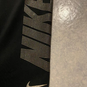 Svarta leggings från Nike - Snygga svarta leggings från Nike med glittrig logga längs benet. Perfekta för träning eller en avslappnad dag. De har en tight passform och är tillverkade i ett stretchigt material för bästa komfort. Knappt andvända. Står ingen storlek i de men skulle gissa på xs/s.