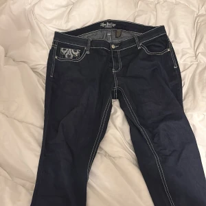 Mörkblå jeansbyxor från Love Indigo - Snygga mörkblå jeansbyxor från Love Indigo med dekorativa bakfickor och kontrastsömmar. Byxorna har en bootcut-stil och är tillverkade i en blandning av rayon, polyester och spandex för extra komfort. Perfekta för en avslappnad look.