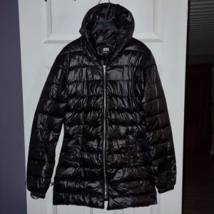 Svart lättviktsjacka från Bik Bok - Säljer en svart lättviktsjacka från Bik Bok i storlek XS. Jackan har en glansig yta och är utrustad med en dragkedja framtill. Nyskick,  endast prövad.