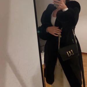 Svart pälsjacka med dragkedja - Snygg svart pälsjacka med dragkedja och långa ärmar. Perfekt för kyliga dagar när du vill hålla stilen. Jackan har en elegant och lyxig look.