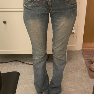 Lågmidjade bootcut jeans - Ett par lågmidjade bootcut jeans i blå med fina detaljer på. Knappen är lite trasig men kan fortfarande stängas men sker att den går upp ibland (se sista bilden)