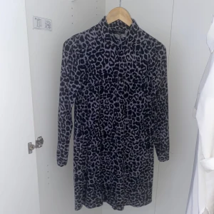 Leopardmönstrad klänning från Essentials - Snygg leopardmönstrad klänning från Essentials med långa ärmar och en klassisk krage. Perfekt för att sticka ut med stil. Klänningen har en normal passform och är gjord i ett mjukt material som känns skönt mot huden.
