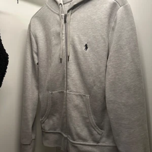 Grå kofta från Ralph Lauren - Säljer en stilren grå hoodie från Ralph Lauren med dragkedja och klassisk logga på bröstet. Nypris 2145 kr säljer den för billigt eftersom behöver pengarna och vill ha den såld snabbt. Skriv via intresse.