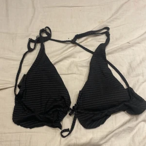 Svart randig bikini från H&M - Snygg svart bikini från H&M med subtila ränder och knytband. Perfekt för en dag på stranden eller vid poolen. Den har en klassisk trekantsform och justerbara band för bästa passform.