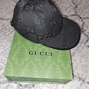 Svart keps från Gucci - Snygg svart keps från Gucci med det ikoniska GG-mönstret. Kepsen har en justerbar rem baktill i skinn för perfekt passform. Perfekt för att ge din outfit en lyxig touch.