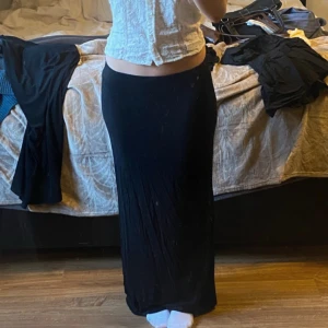 Svart långkjol - Säljer en elegant svart långkjol som passar perfekt för olika tillfällen. Kjolen har en tight passform som framhäver figuren och är tillverkad i ett mjukt och bekvämt material. Perfekt för att skapa en stilren look.