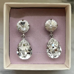Silverfärgade örhängen med stora kristaller - Eleganta silverfärgade örhängen från Caroline Svedbom med stora, gnistrande kristaller i droppform. Perfekta för att ge en lyxig touch till din outfit. Finns tecken på användning, vilket syns i bilderna 🤗