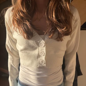 Vit kofta med knappar - Säljer en stilren kort vit kofta med stora knappar framtill. Koftan har en croppad design och långa ärmar.💕snygg både öppen och knäppt😄