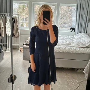 Mörkblå spetsklänning - Säljer en elegant mörkblå klänning i spets med trekvartsärm. Klänningen har en normal passform och når till knäna, perfekt för en stilren look. Den har en rund halsringning och fina spetsdetaljer. Lappen är avklippt men uppskattar storleken till S. den är stretchig i materialet. 