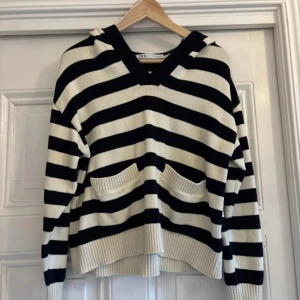 Randig hoodie från Zara - Säljer en snygg randig hoodie från Zara i svart och vitt. Tröjan har en avslappnad passform med långa ärmar och praktiska fickor framtill. Perfekt för en casual look.