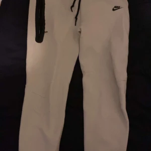 Begie  mjukisbyxor från Nike - Säljer ett begie mjukisbyxor från Nike med svart logga. Byxorna har snörning i midjan för justerbar passform. Perfekta för en avslappnad stil. Vid snabb affär pris säkning