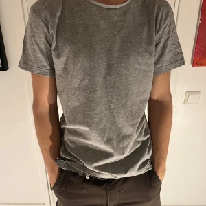 Grå t-shirt från Hampton Republic - Säljer en klassisk grå t-shirt från Hampton Republic. Den är tillverkad i mjuk bomull och har en normal passform med korta ärmar. Perfekt för en avslappnad stil.