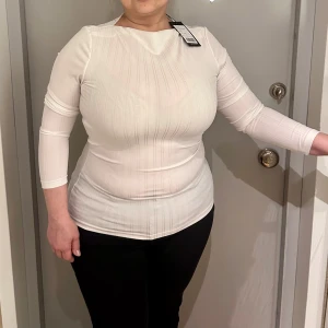 Vit ribbad topp från Zign - Säljer en stilren vit ribbad topp från Zign. Toppen har långa ärmar och en klassisk rund halsringning. Perfekt för en minimalistisk look. Helt ny med tag kvar.