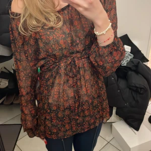 Svart röd blommig blus - Blusen har ett knytband i midjan och ett snyggt mönster i mörka nyanser av rött och svart ❤️Bandet går att knyta fram o bak beroende på hur man vill ha det. Lite Oversized på mig som vanligtvis har S